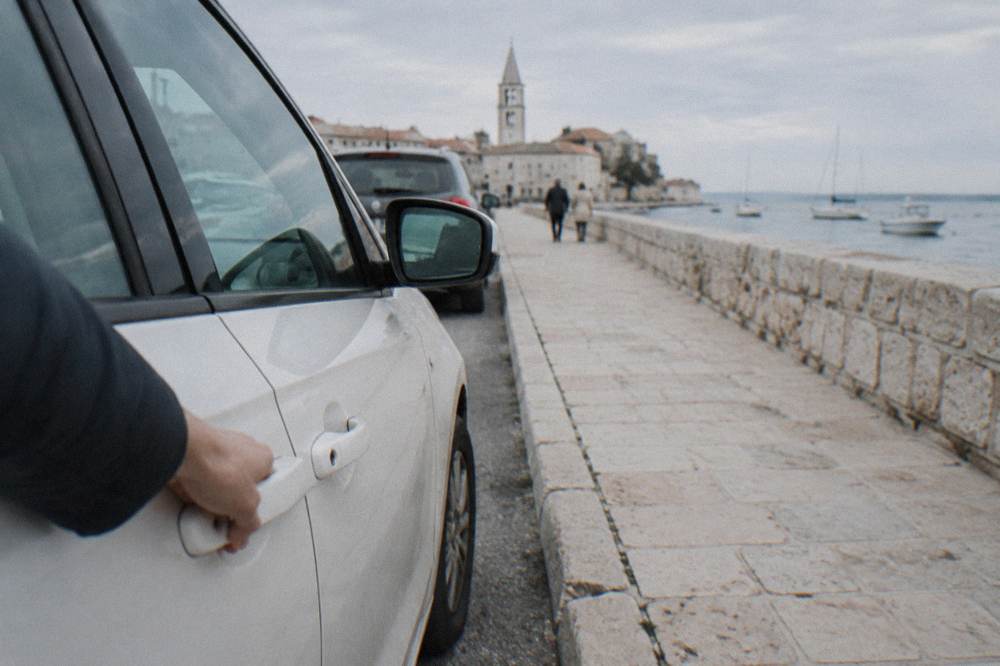 A parked white car at a kerb beside a limestone wall in Zadar.