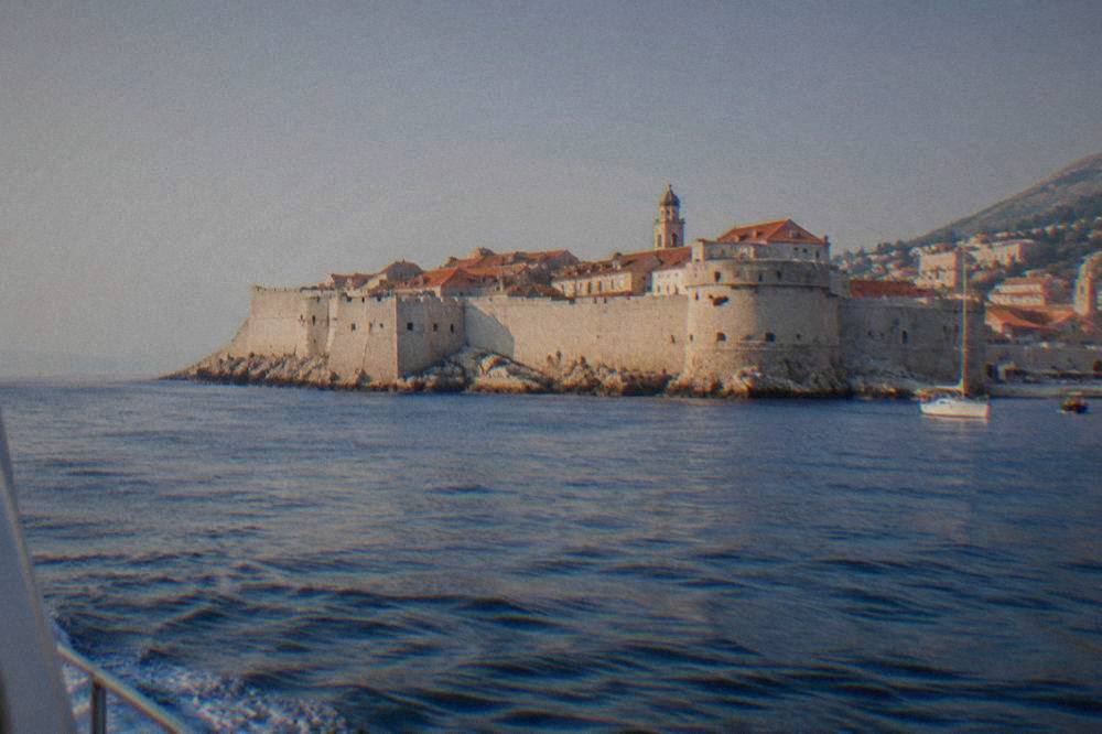 Dubrovnik's walled old town seen from the water with red roofs above deep blue sea.