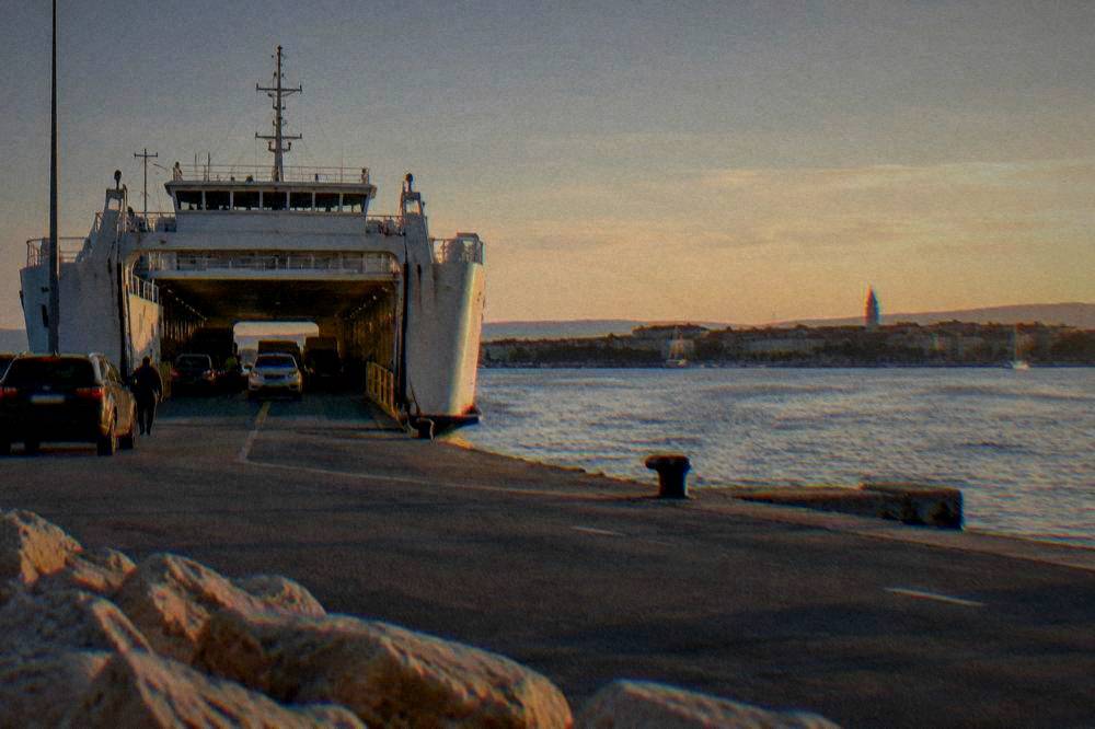 A car ferry at Gaženica port on calm sea with the Zadar waterfront across the bay.