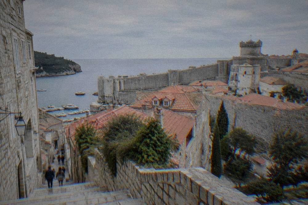 Dubrovnik city walls above a quiet stone street with limestone steps and red roofs.