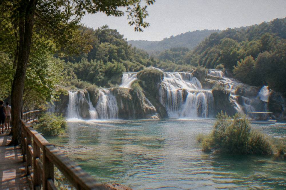 Krka falls over travertine terraces into green pools surrounded by trees.