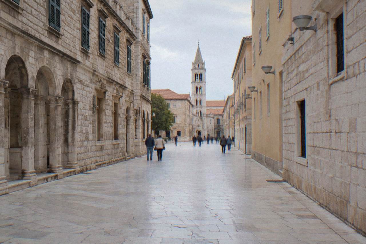 The wide limestone Kalelarga street in Zadar with distant walkers and a bell tower.