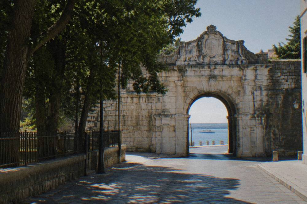 The carved stone Sea Gate arch in a quiet street of Zadar in morning light.
