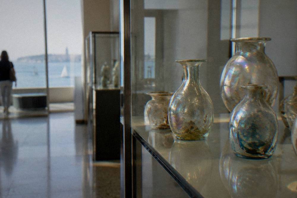 Delicate iridescent ancient glass jars in a softly lit display cabinet.