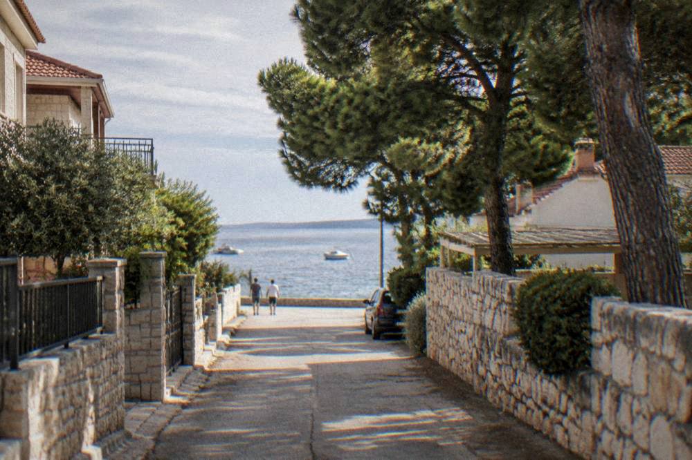 A quiet seaside street at Diklo near Zadar with pines, stone walls and glimpses of sea.