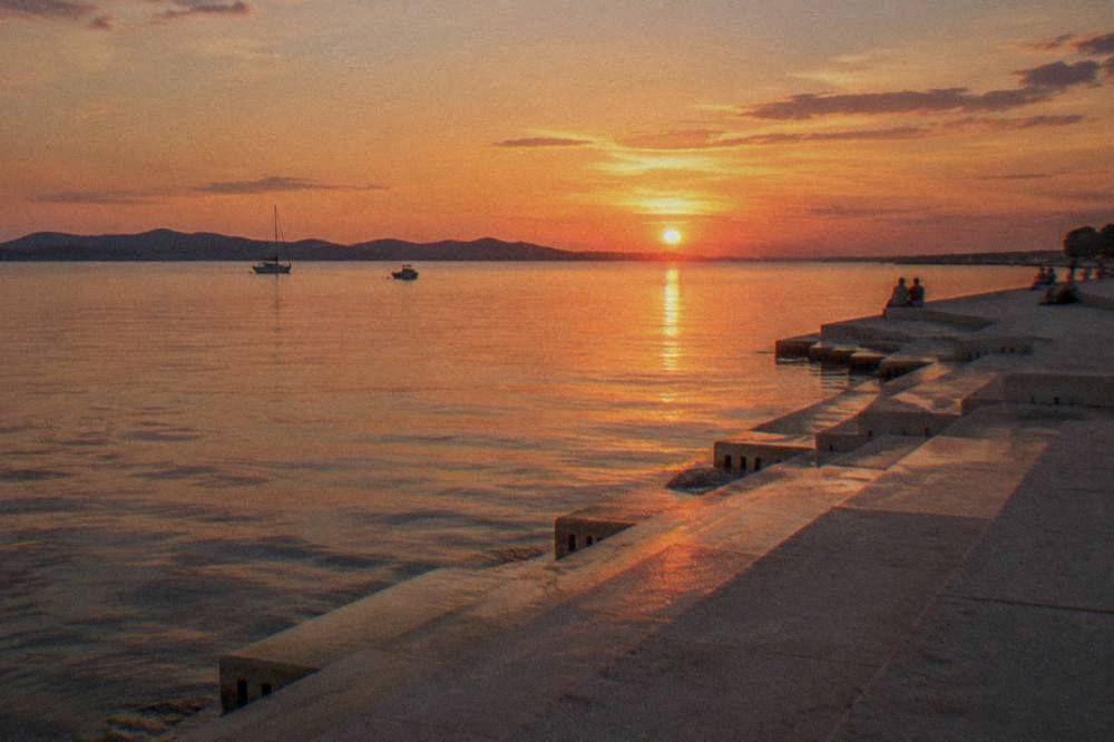 Sea Organ steps at sunset over calm sea in Zadar with tiny distant people.