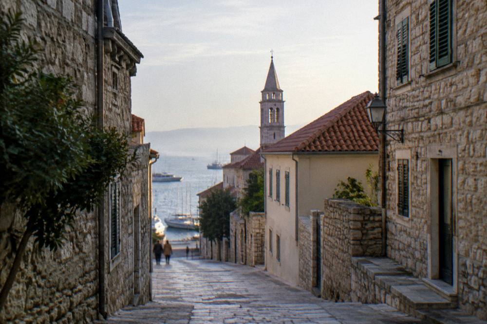 Limestone lanes in Zadar leading toward the sea with a bell tower above.