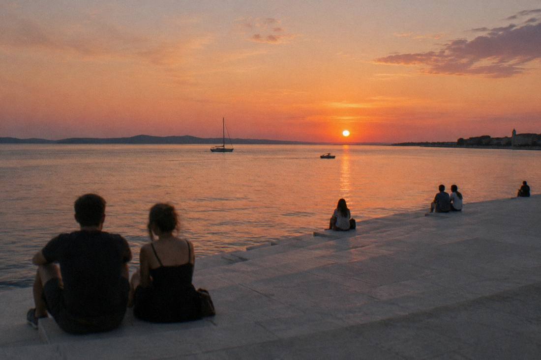 People sitting on the stone steps by the sea at sunset in Zadar