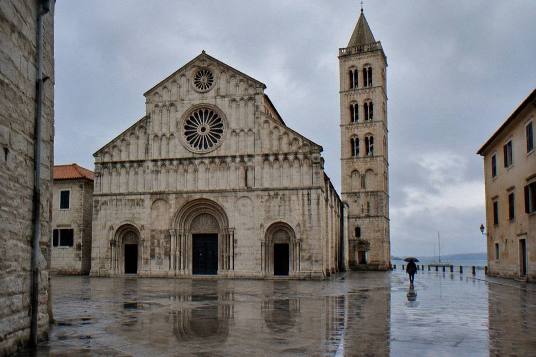 A Romanesque cathedral facade and square bell tower in Zadar on a rainy day with wet paving
