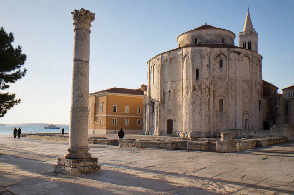 Round pale stone church and a Roman column in the morning forum