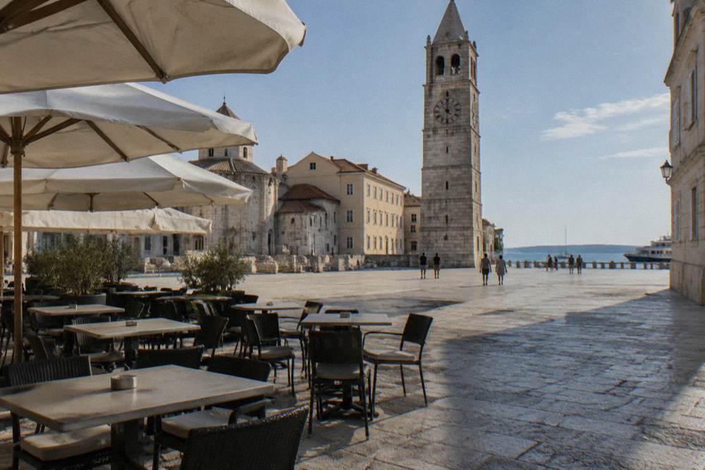 Lunchtime cafe terrace on a stone square beneath a clock tower