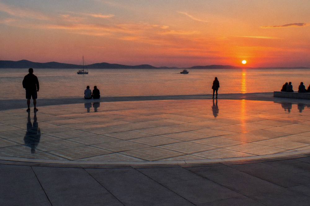 Glass-panel circle on the waterfront at sunset with silhouettes in summer light