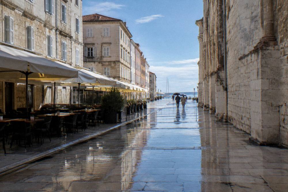 Polished stone main street in light rain with distant umbrellas