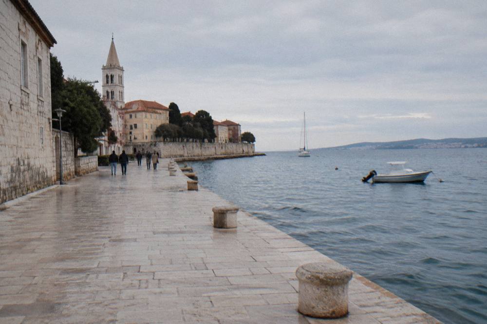 Walkers on a stone promenade between the sea and the Old Town
