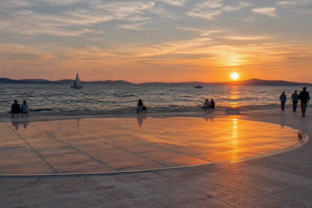 Glass-panel circle glowing orange at sunset over the sea in soft natural light