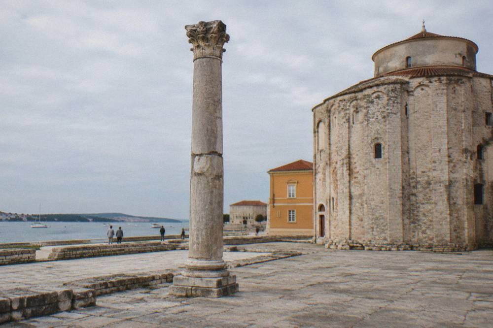 Roman column on ancient paving beside a round stone church