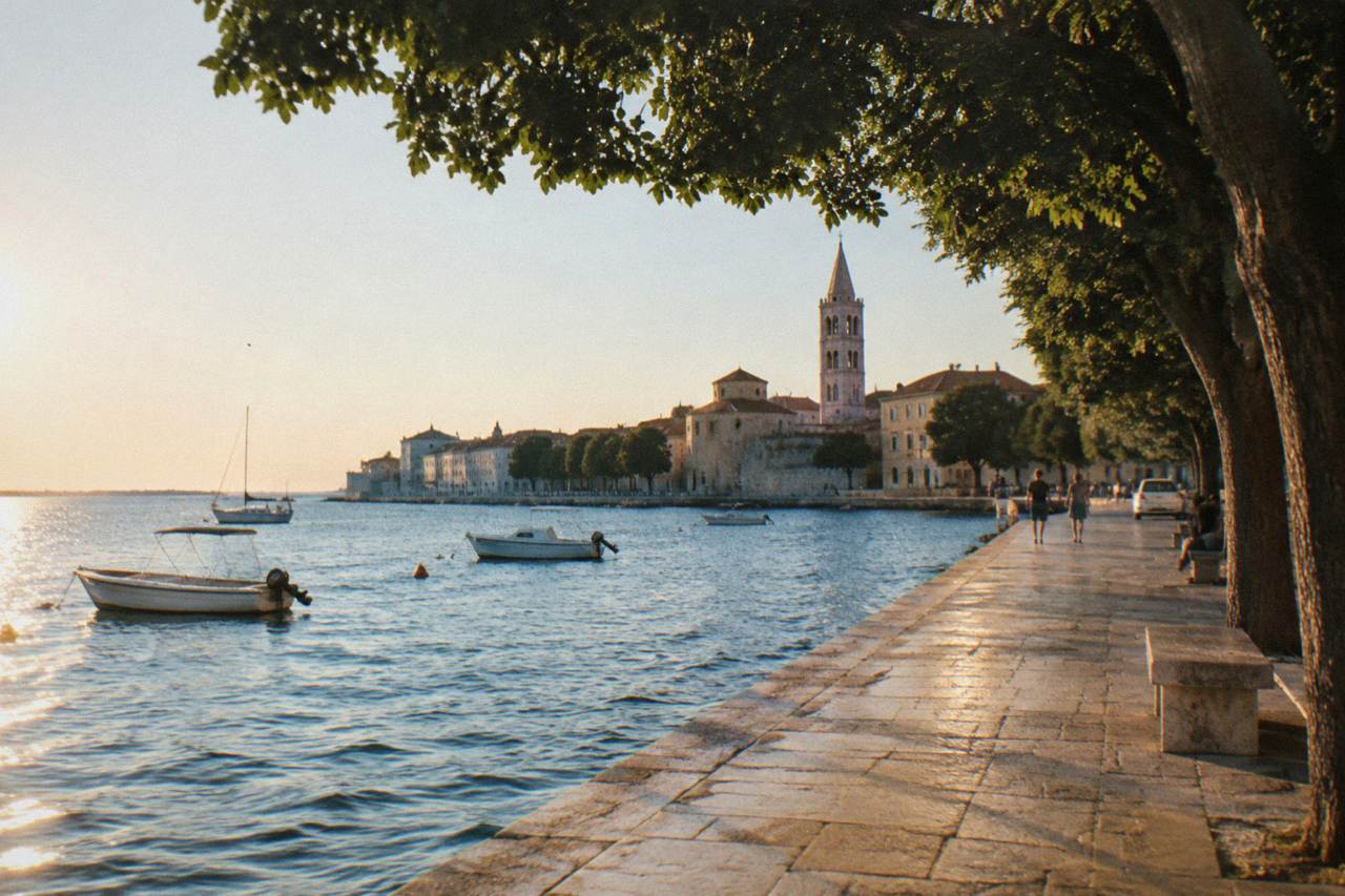 Zadar waterfront at golden hour with a bell tower and a distant parked car