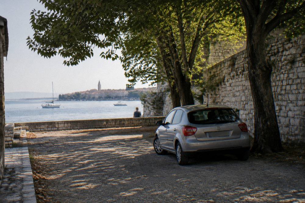 Car parked in a quiet lot beside the Old Town walls under trees