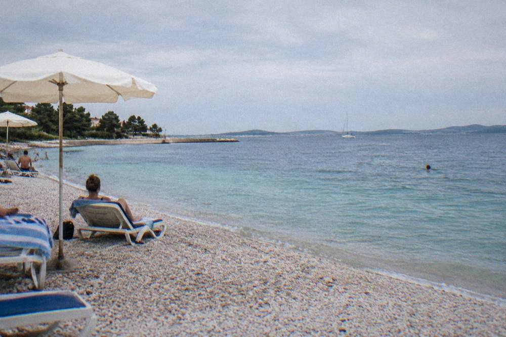 Pebble beach with clear turquoise water and distant swimmer on a clear day