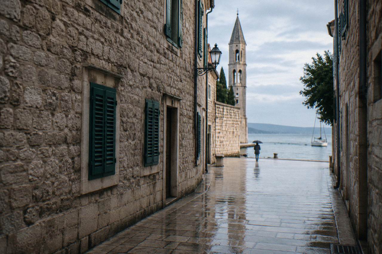 Wet stone Old Town lane after rain with a distant umbrella
