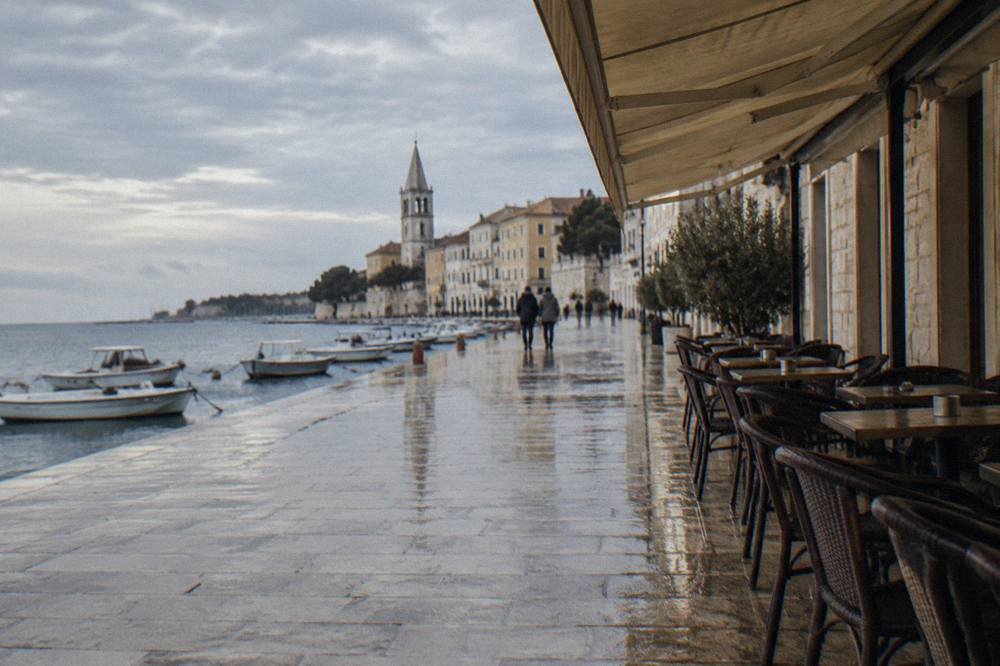 Cafe awning over empty chairs on wet limestone paving on a clear day