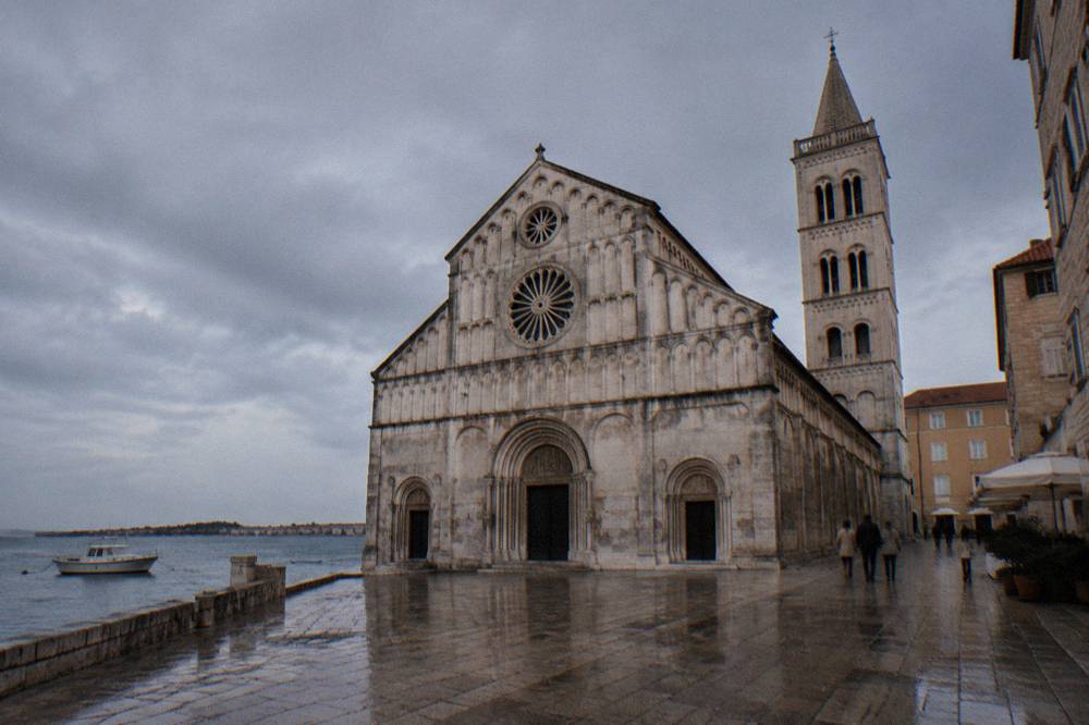 Cathedral facade under a grey sky with wet paving in summer light