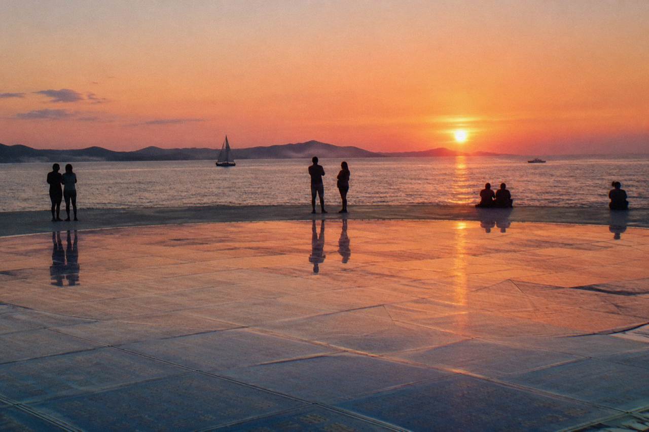 Glass-panel circle on the waterfront at sunset with silhouettes in summer light