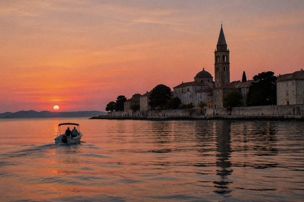 Boat on calm water off the Old Town at sunset with tower silhouette